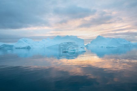 Foto de Icebergs al atardecer. Naturaleza y paisajes de Groenlandia. Disko bay. Groenlandia Occidental. Sol de medianoche de verano y témpanos. Gran hielo azul en el fiordo de hielo. Afectados por el cambio climático y el calentamiento global - Imagen libre de derechos
