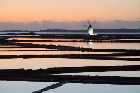 Photo for Sunset at Windmill in the salt evaporation pond in Marsala, Sicily island, Italy Trapani salt flats and old windmill in Sicily. View in beautiful sunny day. - Royalty Free Image