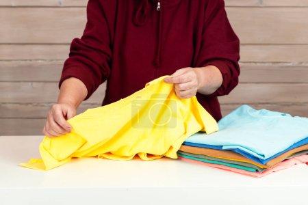 Photo for A woman folds several multi-colored t-shirts. Preparing clothes for donation to charity. Conscious consumption. Disposal of unused clothing. slow fashion - Royalty Free Image