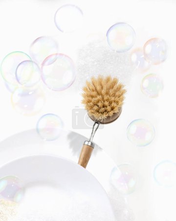 Photo for Eco-friendly bamboo dishwashing brush with long wooden handle. Creative concept cleaning with soap bubbles. - Royalty Free Image