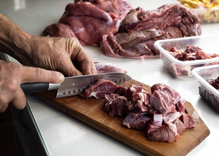 A man prepares various raw meats, bones and offal for freezing in portion containers. BARF Biologically Appropriate Raw Food for Dogs and Cats. Animal food packaging.