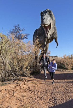 Foto de Moab, Utah, Estados Unidos - 22 de noviembre de 2021: réplica de dinosaurio T rex con personas huyendo y asustadas en el rastro de dinosaurios Moab Giants - Imagen libre de derechos