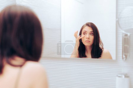 Téléchargez les photos : Femme appliquant un produit cosmétique sous ses yeux dans le miroir - en image libre de droit