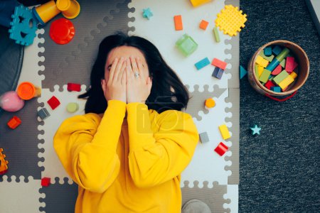 Photo for Stressed Mom Sitting on the Messy Floor Surrounded by Toys - Royalty Free Image