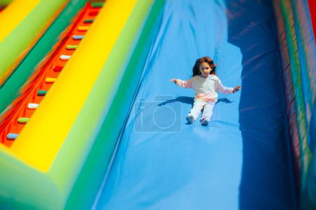 Photo for Happy Girl Playing on a Huge Inflatable Slide in Amusement Park - Royalty Free Image