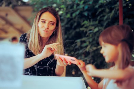 Photo for Mother and Daughter Fighting over a Phone at the Restaurant - Royalty Free Image