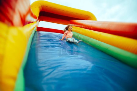 Photo for Scared Little Girl Playing on an Inflatable Slide in Amusement Park - Royalty Free Image