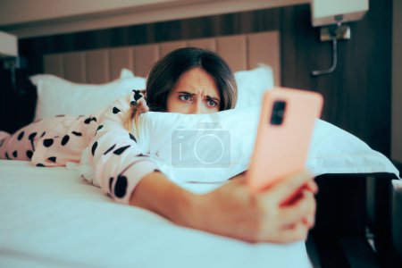 Besorgte Frau blickt auf ihr Handy, das im Bett liegt 