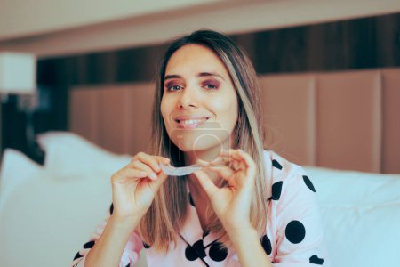 Photo for Woman in Bed Wearing Pajamas Holding Clear Retainer - Royalty Free Image