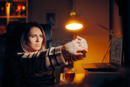 Téléchargez les photos : Femme étirant les bras Travaillant sur son ordinateur portable tard dans la nuit - en image libre de droit