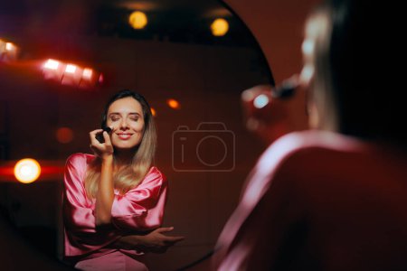 Foto de Mujer usando iluminador en sus pómulos mirándose en el espejo - Imagen libre de derechos
