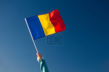 Foto de Mano que renuncia a una bandera rumana en un cielo azul - Imagen libre de derechos