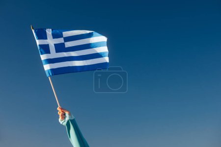 Foto de Mano que renuncia a una bandera griega en un cielo azul - Imagen libre de derechos