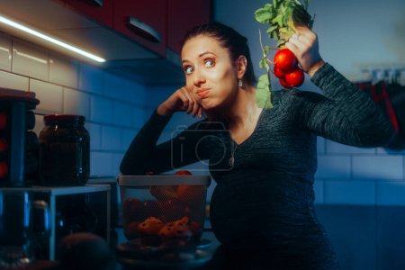 Foto de Mujer embarazada sosteniendo un manojo de rábanos en la cocina - Imagen libre de derechos