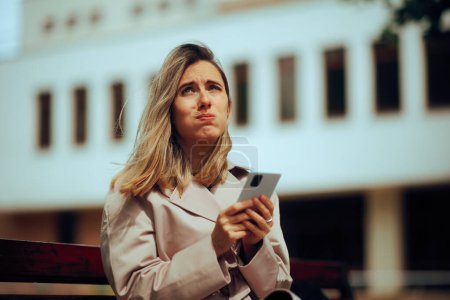 Foto de Mujer estresada revisando su teléfono esperando en un banco - Imagen libre de derechos