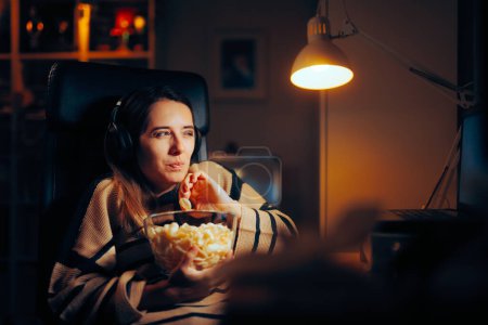 Foto de Mujer divertida comiendo patatas fritas viendo un espectáculo en su ordenador portátil - Imagen libre de derechos