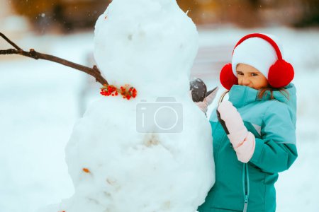 Téléchargez les photos : Petite fille jouant avec un bonhomme de neige se sentant froid - en image libre de droit