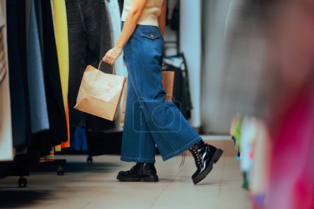 Téléchargez les photos : Shopper tenant un sac en papier marchant dans un magasin de vêtements - en image libre de droit