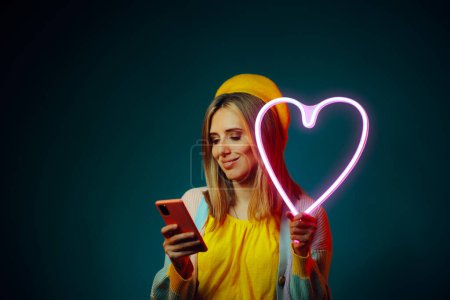 Téléchargez les photos : Happy Woman Vérification d'une application de rencontre en ligne Holding Neon Heart - en image libre de droit