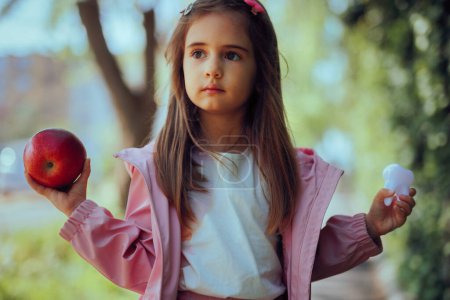 Kleines Mädchen hält einen Apfel und ein weißes gesundes Zahnspielzeug