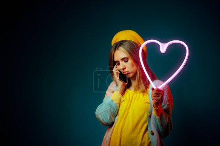 Traurige Frau telefoniert mit neonfarbenem Herzen