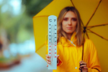 Frau zeigt an einem regnerischen Tag ein Thermometer im Freien