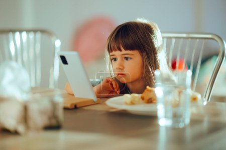Kleines Mädchen schaut während des Essens Cartoons auf dem Smartphone