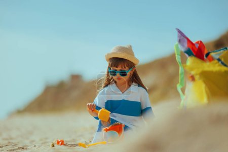 Little Girl Plays with Spatula and Bucket in the Sand on a Beach