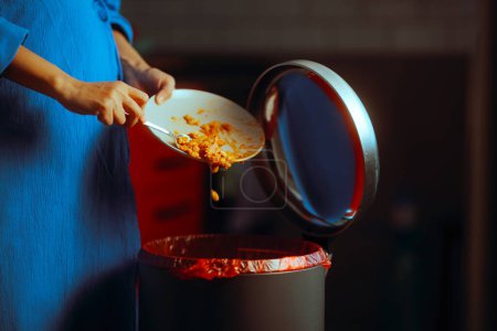 Téléchargez les photos : Femme jetant hors dîner restes de nourriture dans la poubelle - en image libre de droit