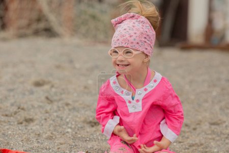 Photo for Little girl with Down syndrome sits on the summer coast - Royalty Free Image