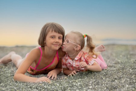 Photo for Portrait of a beautiful girl with a lovely little sister with Down syndrome on the beach - Royalty Free Image