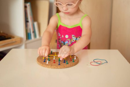 Photo for A girl with Down syndrome trains fine motor skills. Stretch - Royalty Free Image