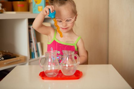 Téléchargez les photos : A girl with Down's syndrome learns to pour water from pitcher to pitcher. Early development - en image libre de droit