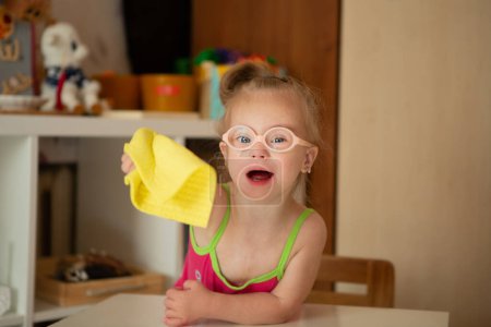 Téléchargez les photos : A girl with Down syndrome learns to clean up after games. wipe the table - en image libre de droit