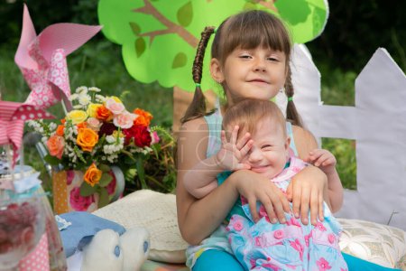 Téléchargez les photos : Portrait of a beautiful girl with a lovely little sister with Down syndrome in the park - en image libre de droit