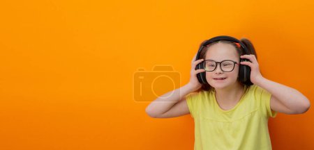 Photo for Girl with Down syndrome listens to music. Orange background. Banner - Royalty Free Image