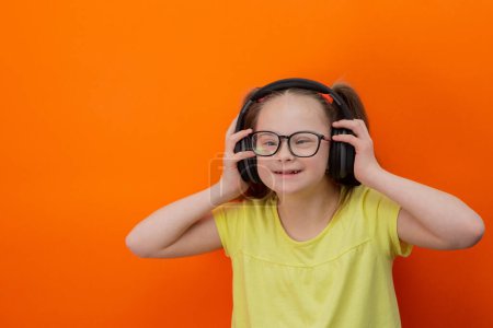 Photo for Girl with Down syndrome listens to music. Orange background - Royalty Free Image