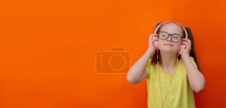 Téléchargez les photos : Girl with Down syndrome listens to music. Orange background. Banner - en image libre de droit