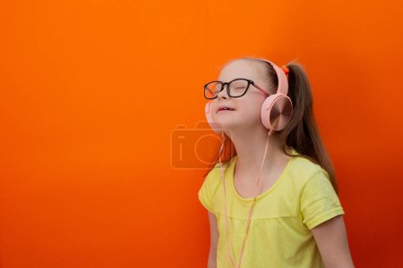 Téléchargez les photos : Girl with Down syndrome listens to music. Orange background - en image libre de droit