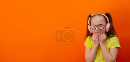 Téléchargez les photos : Girl with Down syndrome listens to music. Orange background. Banner - en image libre de droit