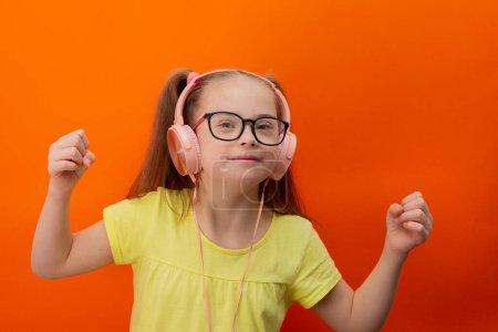 Téléchargez les photos : Girl with Down syndrome listens to music. Orange background - en image libre de droit