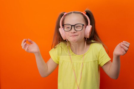 Photo for Girl with Down syndrome listens to music. Orange background - Royalty Free Image