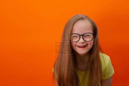 Happy girl with Down syndrome. Having fun, laughing. Funny pigtails. Studio. Portrait on a orange background