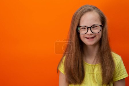 Photo for Happy girl with Down syndrome. Having fun, laughing. Funny pigtails. Studio. Portrait on a orange background - Royalty Free Image