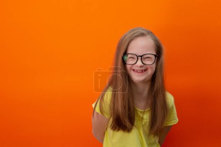 Téléchargez les photos : Happy girl with Down syndrome. Having fun, laughing. Funny pigtails. Studio. Portrait on a orange background - en image libre de droit