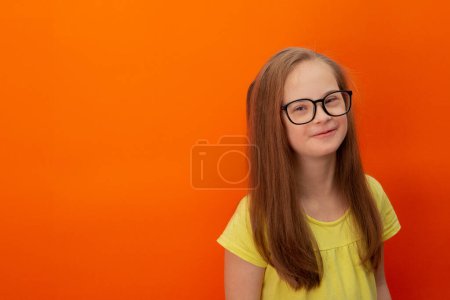 Téléchargez les photos : Happy girl with Down syndrome. Having fun, laughing. Funny pigtails. Studio. Portrait on a orange background - en image libre de droit