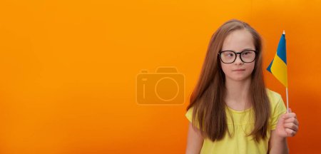 Téléchargez les photos : A girl with Down syndrome holds the flag of Ukraine. orange background. Banner - en image libre de droit