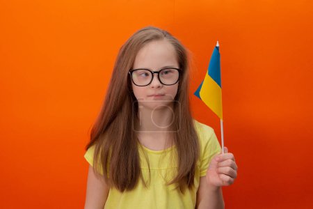 Téléchargez les photos : A girl with Down syndrome holds the flag of Ukraine. orange background - en image libre de droit