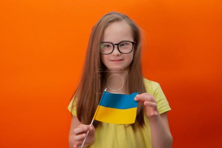 Téléchargez les photos : A girl with Down syndrome holds the flag of Ukraine. orange background - en image libre de droit