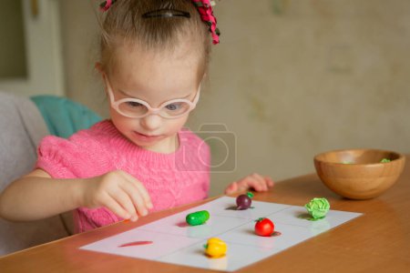 Photo for A beautiful smart girl with Down syndrome learns to sort. Vegetables - Royalty Free Image